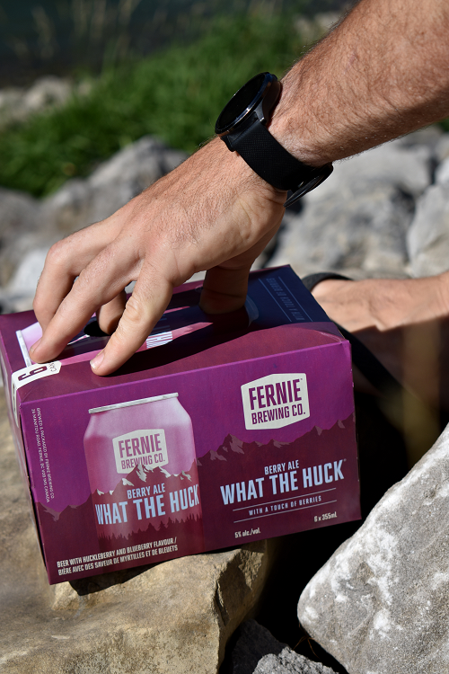 A man picking up a six-pack of What the Huck® Berry Ale off a rock.
