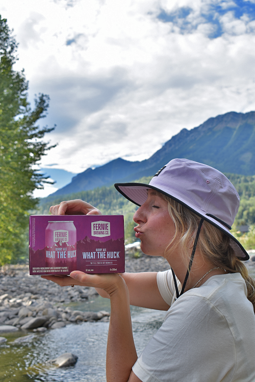 A girl holding a box of What the Huck® Berry Ale next to her face.