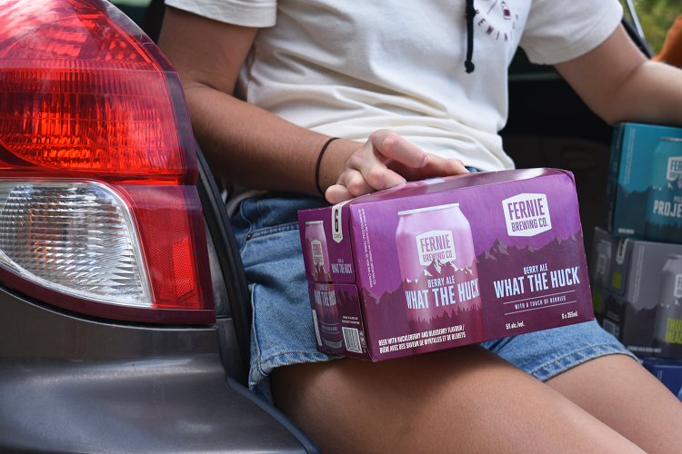 A woman holding a six-pack of What the Huck® Berry Ale on her lap.