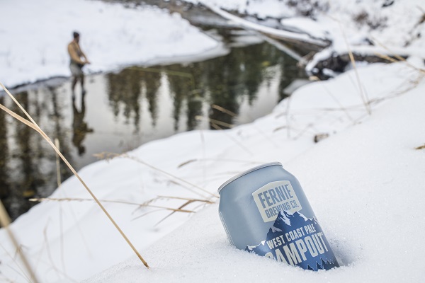 a can of campout in the snow by a river with someone fishing in the background