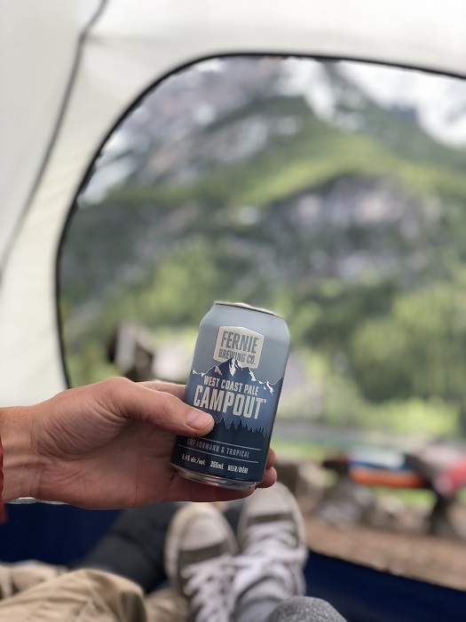 A hand holding a can of campout in a tent