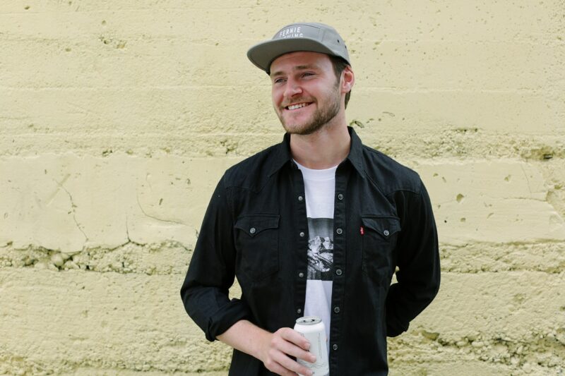 Man wearing a black FBC denim shirt over a white t-shirt holding a beer.