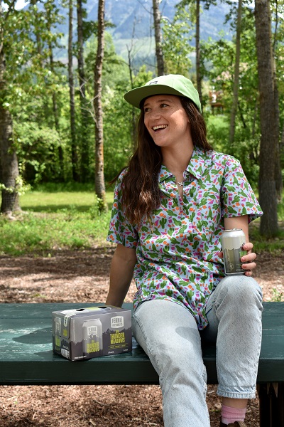 a girl laughing sitting on a picnic table with a can of beer in hand