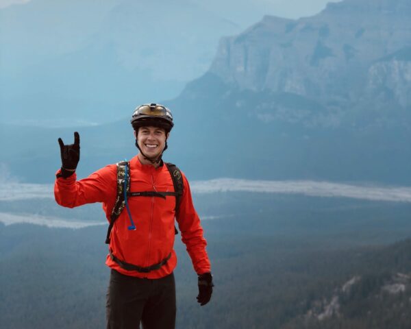 Man smiling in bike helmet and red jacket on mountain.