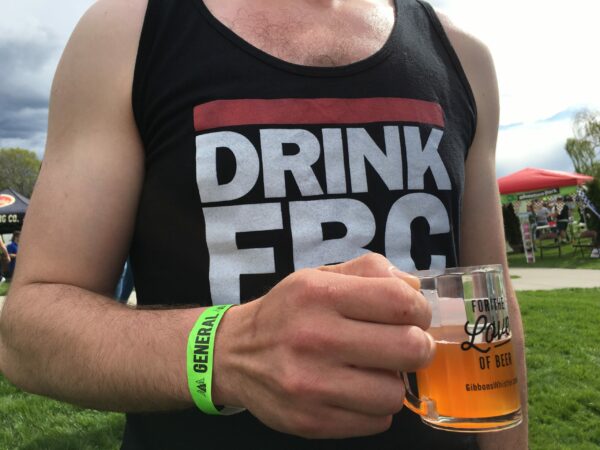 Man wearing black tank at festival with beer.