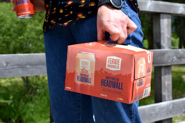 A person holding a 6 pack of Headwall Hazy Pale Ale