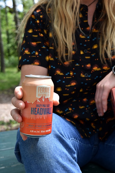 A woman's hand holding a can of Headwall Hazy Pale Ale in the summer sun