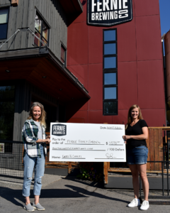 two women holding up a big cheque in front of the brewery