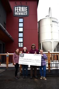 Four poople holding up a donation cheque in front of a brewery