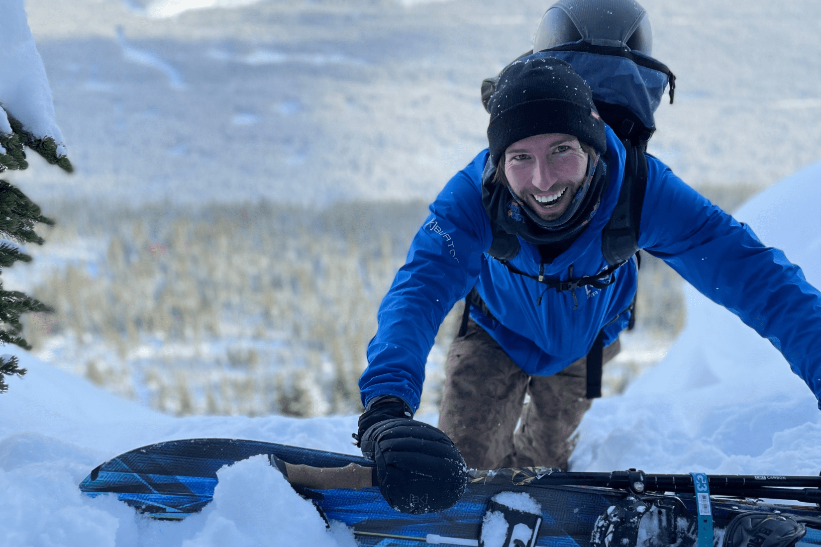 A man outside in winter smiling and holding a snowboard.