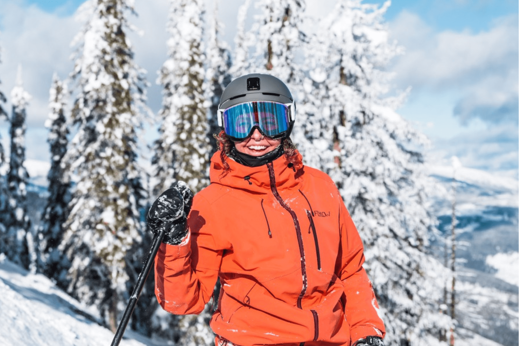 A woman wearing ski gear on a mountain smiling.